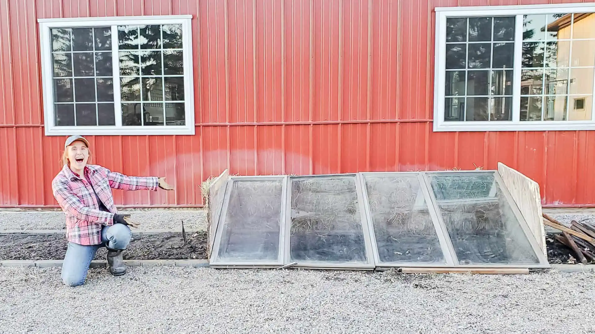 Ashley Headrick kneeling next to garden cold frames made from old windows and hay bales